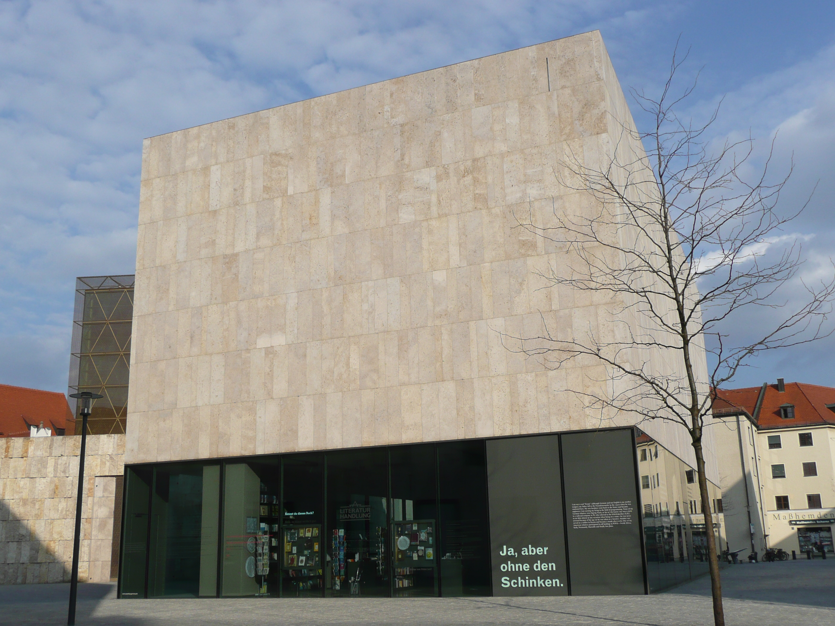 Square building made of light-coloured stone with a glass ground floor and the inscription ‘Yes, but without the ham’