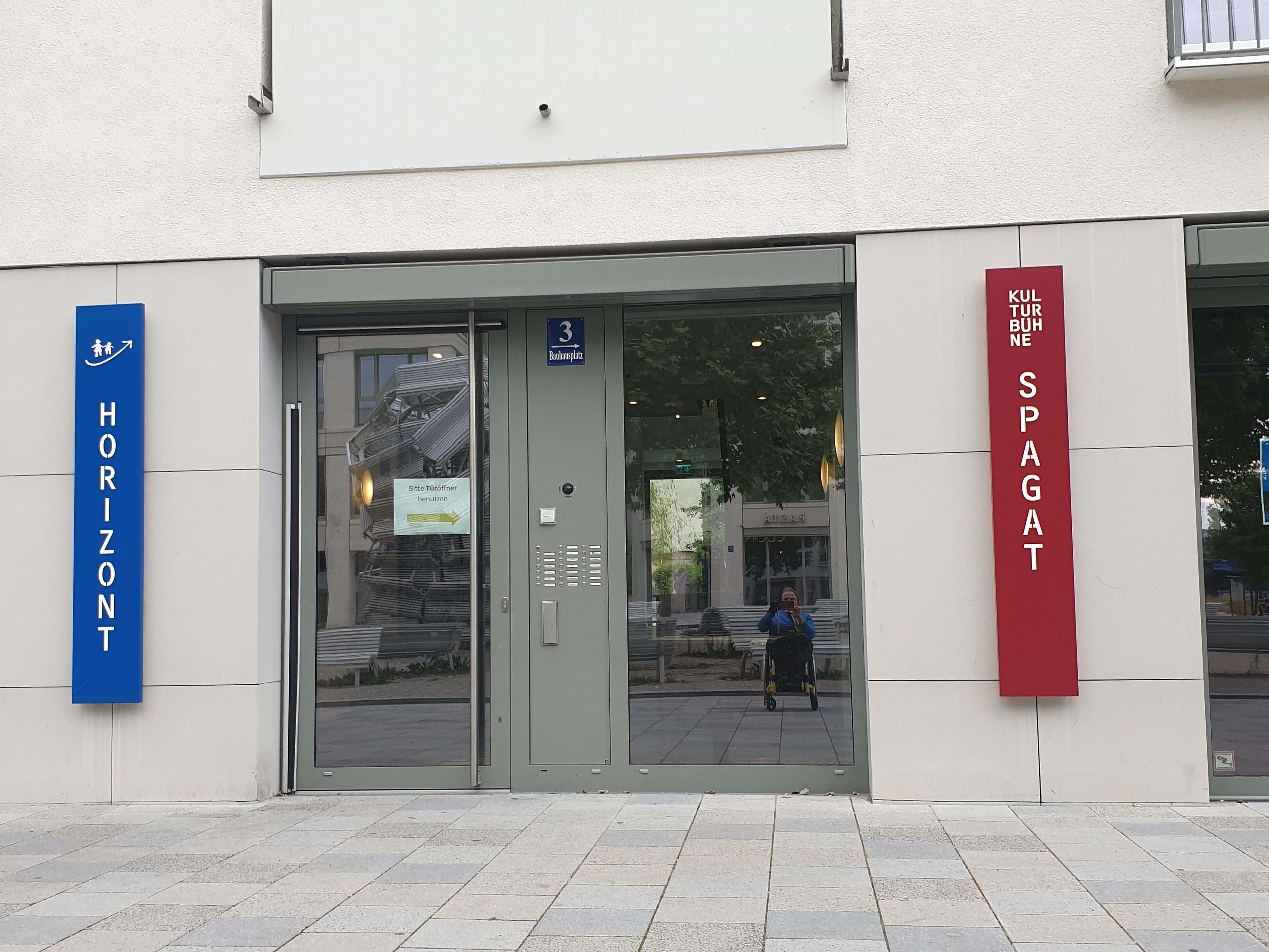 Eingangstüre ebenerdig links davon blaues Schild Horizont rechts davon rotes Schild Kulturbühne Spagat