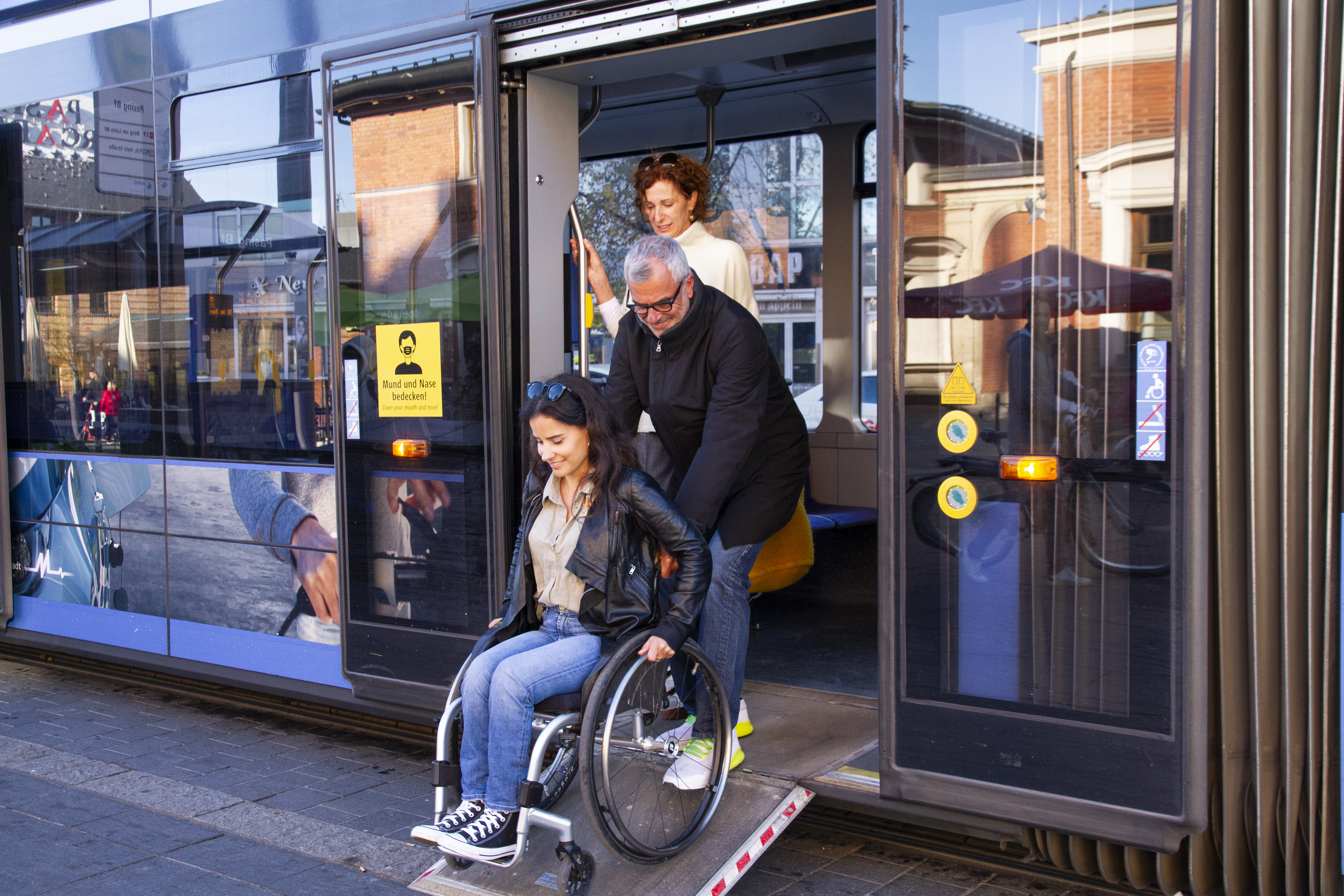 Ein Mann hilft einer Frau im Rollstuhl beim Verlassen eines Busses über eine buseigene Rampe