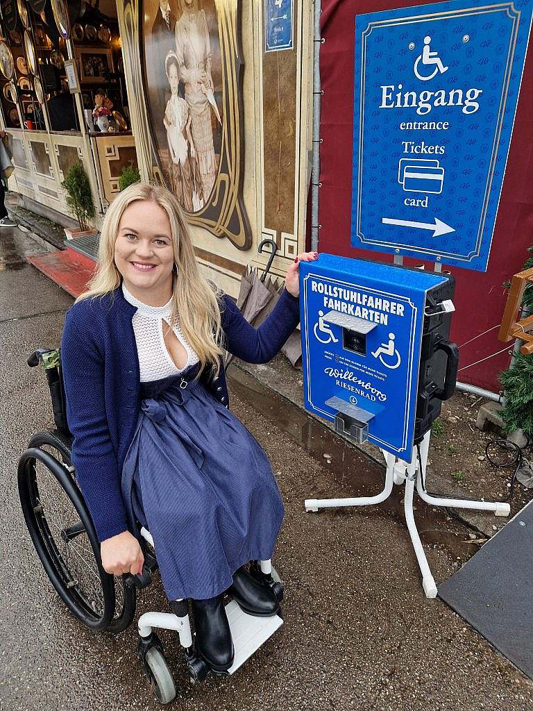 Frau im Rollstuhl am Extra-Fahrkartenautomaten beim Riesenrad