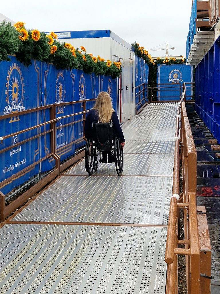 Frau im Rollstuhl fährt die Rampe zum Riesenrad hoch