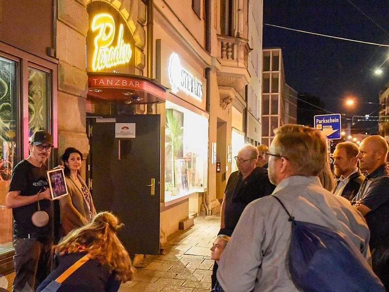 Mann mit Schild vor der Brust vor einer ihm zugewandten Gruppe