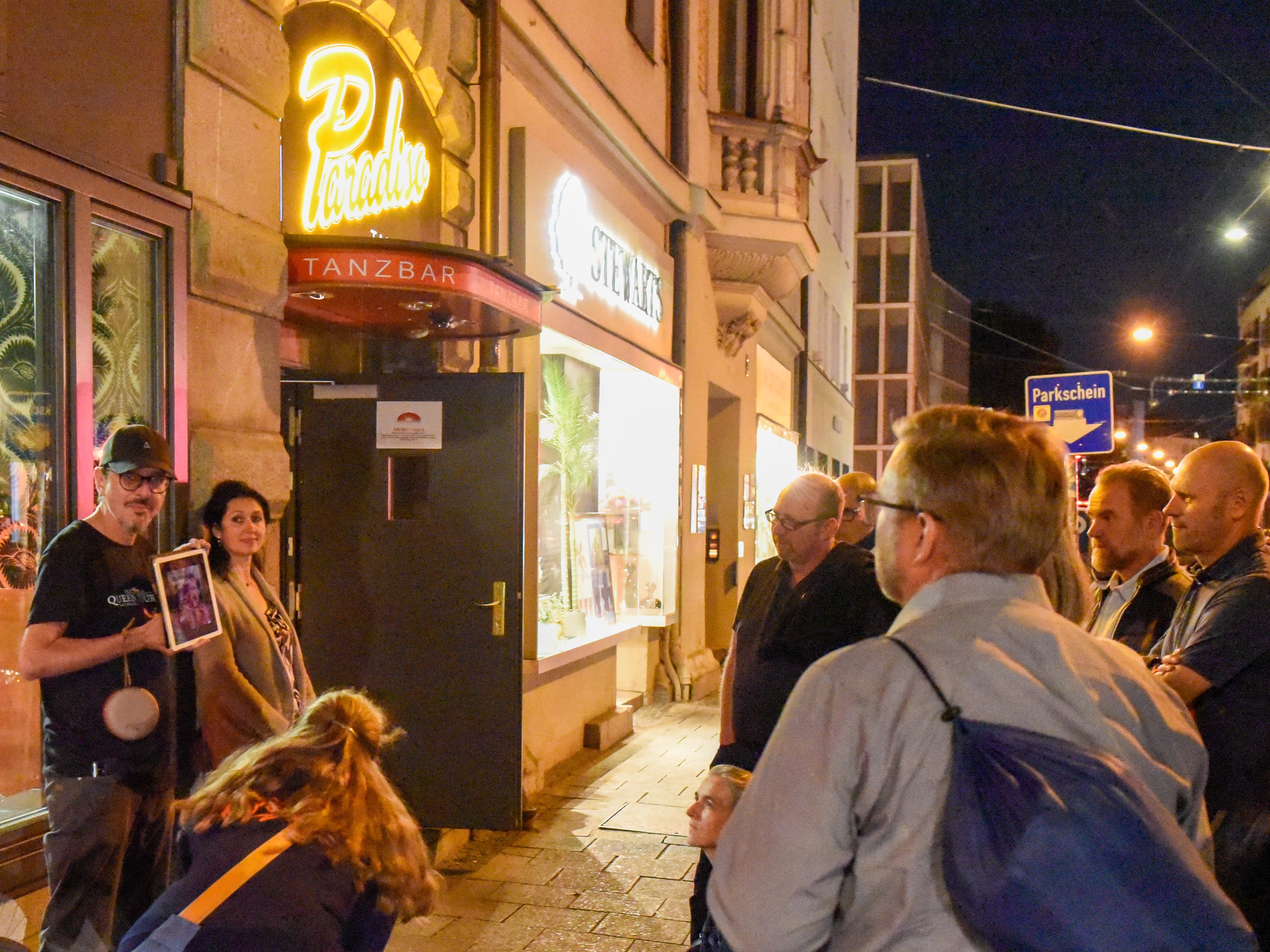 Mann mit Schild vor der Brust vor einer ihm zugewandten Gruppe