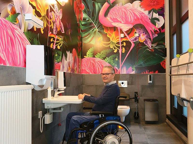 Interior of ‘Toilet for All’, man in wheelchair in front of washbasin