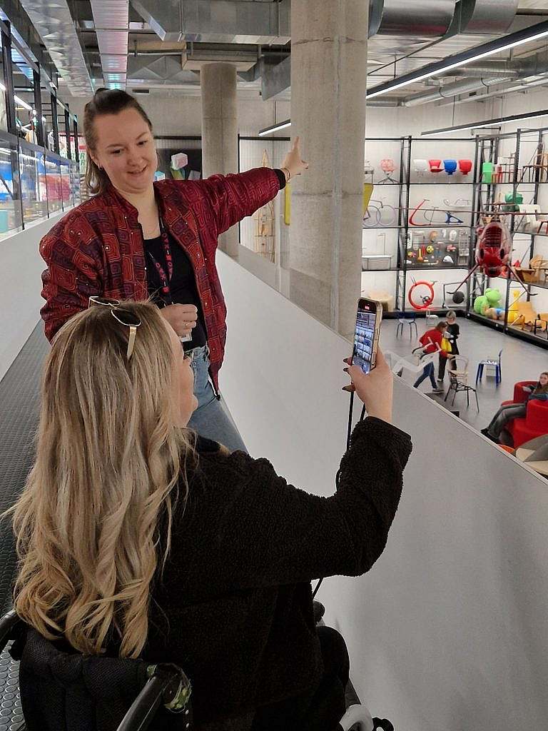 Woman standing next to woman in wheelchair pointing at something