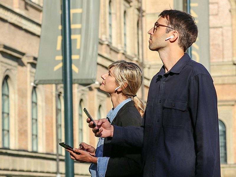 Two people wearing headphones and holding smartphones in front of a building