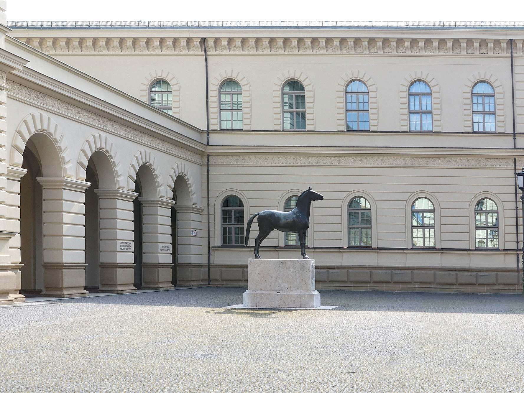 Gebäude mit Bogengang, davor Pferdestatue